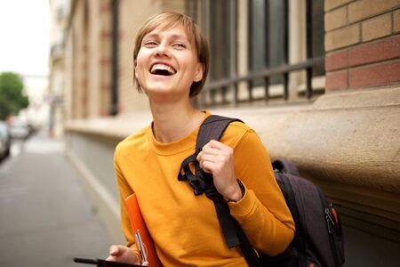 Portrait of female college student with bag laughing outsideの写真素材