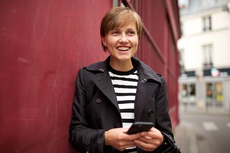 Portrait of happy young woman standing outside with mobile phone