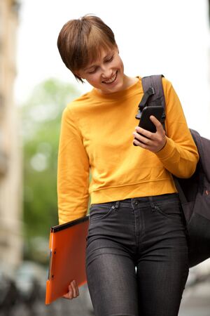 Portrait of young woman with short hair walking outside and looking at mobile phone