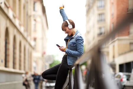Side portrait of happy young woman looking at mobile phone with hand raised upの写真素材