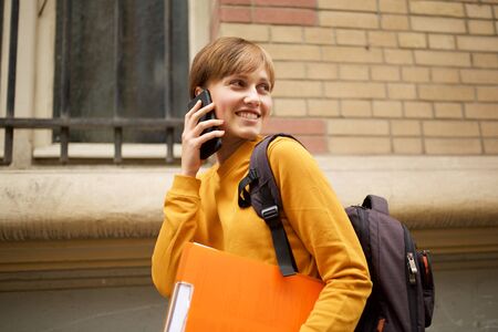 Side portrait of happy female college student talking with mobile phoneの写真素材