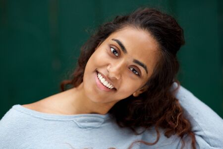 Close up portrait of beautiful young Indian woman smiling against green background with hand in hair