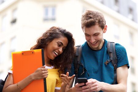 Portrait of smiling college students looking at mobile phone while in cityの写真素材