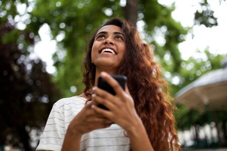 Portrait of happy young woman holding cellphone and looking upの写真素材