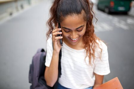 Close up portrait of beautiful young woman smiling and talking with cellphone on streetの写真素材