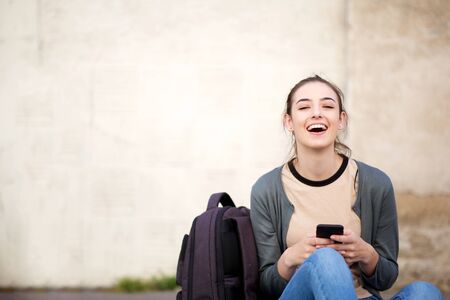 Portrait of laughing female student sitting outside with mobile phone