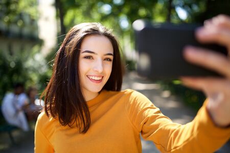 Portrait of beautiful young woman taking selfie photo with mobile phone in the park