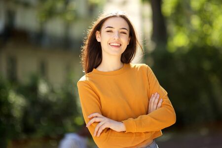 Portrait of smiling young woman with arms crossed in the park