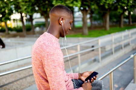 Side portrait of young african american man listening to music with headphones and mobile phone