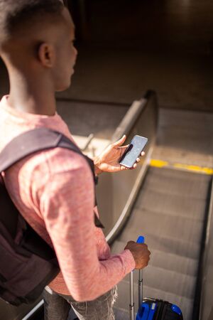 Portrait from behind of young man going down escalator with mobile phone