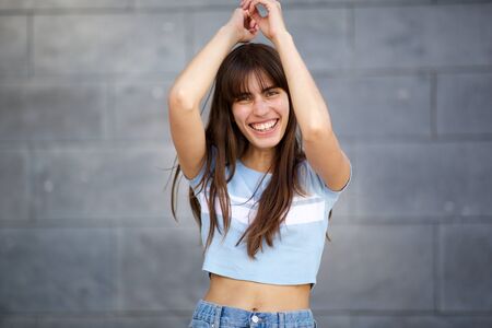 Close up portrait of young woman long hair laughing with arms raised against gray background