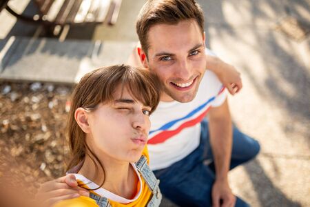 Portrait of smiling boyfriend and cute girlfriend taking selfie outsideの写真素材