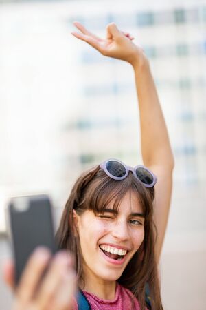 Close up portrait of happy woman with one arm raised taking selfie with cellphoneの写真素材