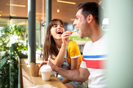 Portrait of fun couple sitting at restaurant and eating food togetherの写真素材
