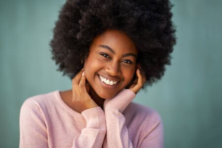 Close up front portrait of beautiful smiling young african american woman with afro and hand on faceの写真素材