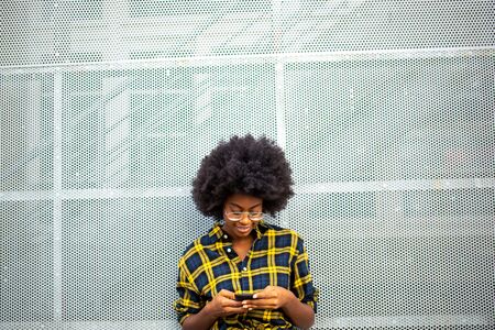 Front portrait of stylish young african american woman with afro looking at mobile phoneの写真素材