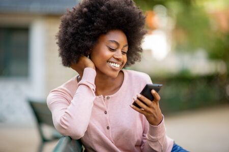 Close up portrait of smiling young african american lady with afro hair looking at mobile phoneの写真素材