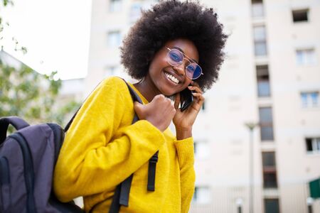 Side portrait happy young african american woman with glasses and bag walking in city and talking with phoneの写真素材