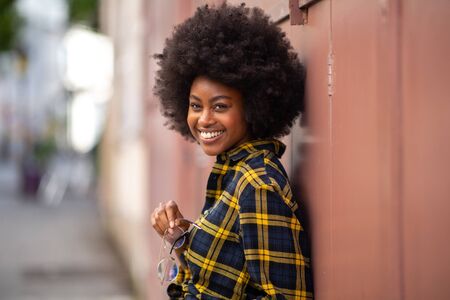 Portrait of smiling young african american woman with afro hair standing outside and holding glassesの写真素材