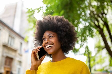 Portrait  of attractive young african woman smiling and talking with cellphone outsideの写真素材