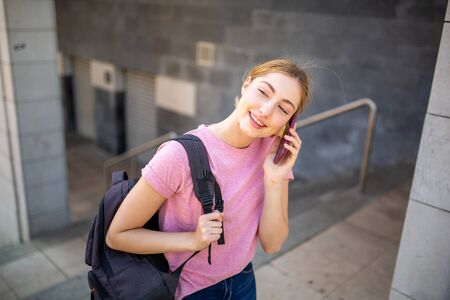 Portrait of happy teenager student walking outside on campus talking with cellphone