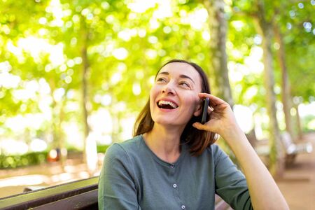 Portrait smiling middle aged woman sitting in park talking with mobile phoneの写真素材