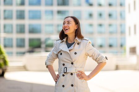 Portrait of laughing older woman standing outside in city with hands on hipの写真素材