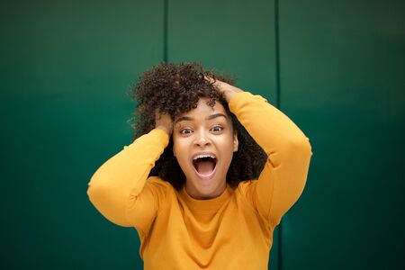 Close up portrait of surprised young african american woman with hands in hair and mouth openの写真素材
