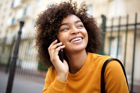 Close up portrait of happy african american young woman talking with cellphone outside in city