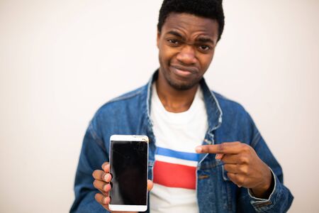 Close up portrait of worried young man pointing to mobile phone screenの写真素材