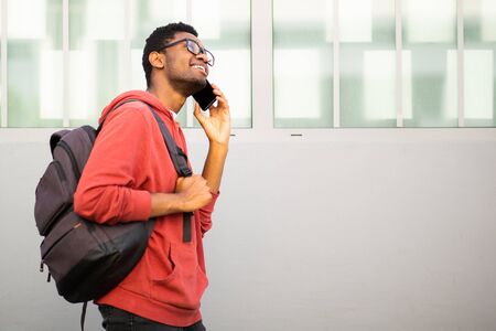 Side portrait african american college student walking and talking with mobile phone