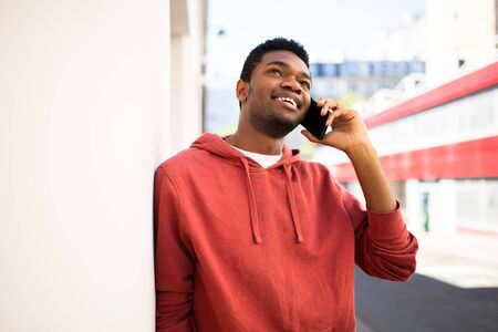 Portrait happy african american man leaning against wall talking with mobile phone outside