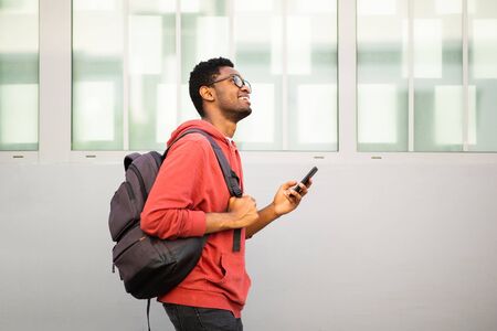 Side portrait african american college student walking with mobile phone and bag