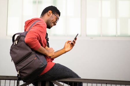 Side portrait of young african american man sitting outside looking at mobile phone
