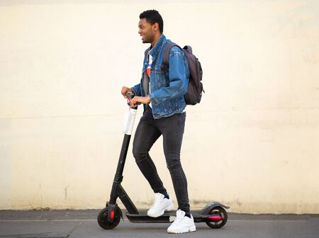 Full body side portrait happy african American guy on mobile scooter on streetの写真素材
