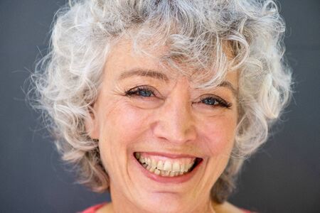 Close up front portrait of attractive older woman smiling with gray curly hairの写真素材