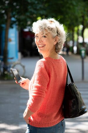 Portrait from behind of middle aged woman walking with mobile phone and bag in city