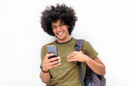 Portrait of cool young guy with bag looking at cellphone and smiling