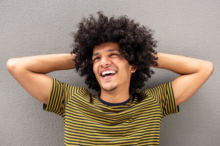 Close up portrait of happy young modern arab man relaxing with hands behind head by wallの写真素材