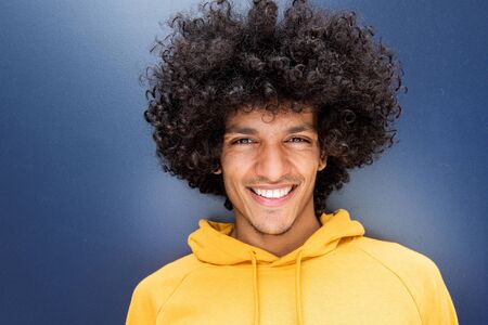 Close up front portrait of handsome young North African man with afro hairstyle smiling against blue backgroundの写真素材