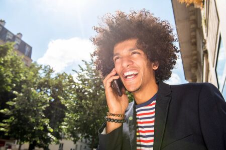 Close up portrait of happy young arab guy with afro hair talking with cellphone outside
