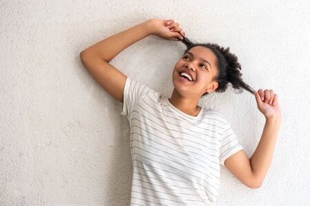 portrait cheerful young african american girl pulling hair by white wallの写真素材