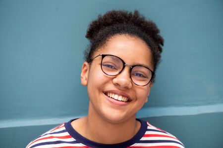Close up portrait of smiling young mixed race girl with glasses against blue wall