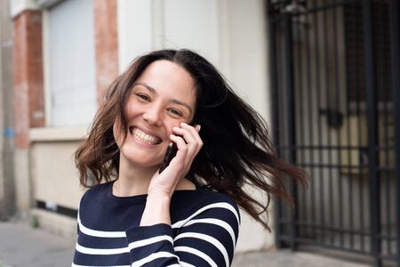Close up portrait of happy young woman turning around and talking with cellphone in city