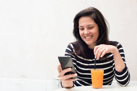 Portrait happy young woman sitting at cafe table looking at cellphone