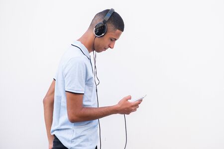 Side portrait of North African man listening to music with headphones and mobile phone by white backgroundの写真素材