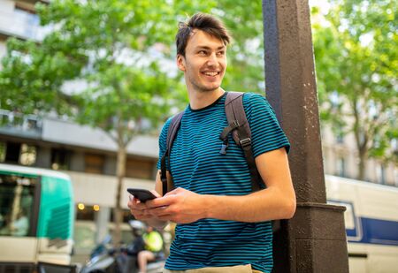 Portrait smiling young man in city holding mobile phone in handの写真素材