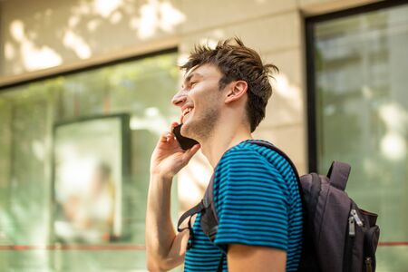 Side portrait of happy young man in city talking with mobile phone