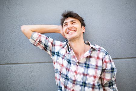 Close up portrait of happy young man looking up with hand behind head by gray wallの写真素材