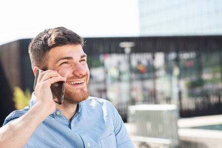 Side portrait of happy young man with beard talking on cellphone outside cityの写真素材